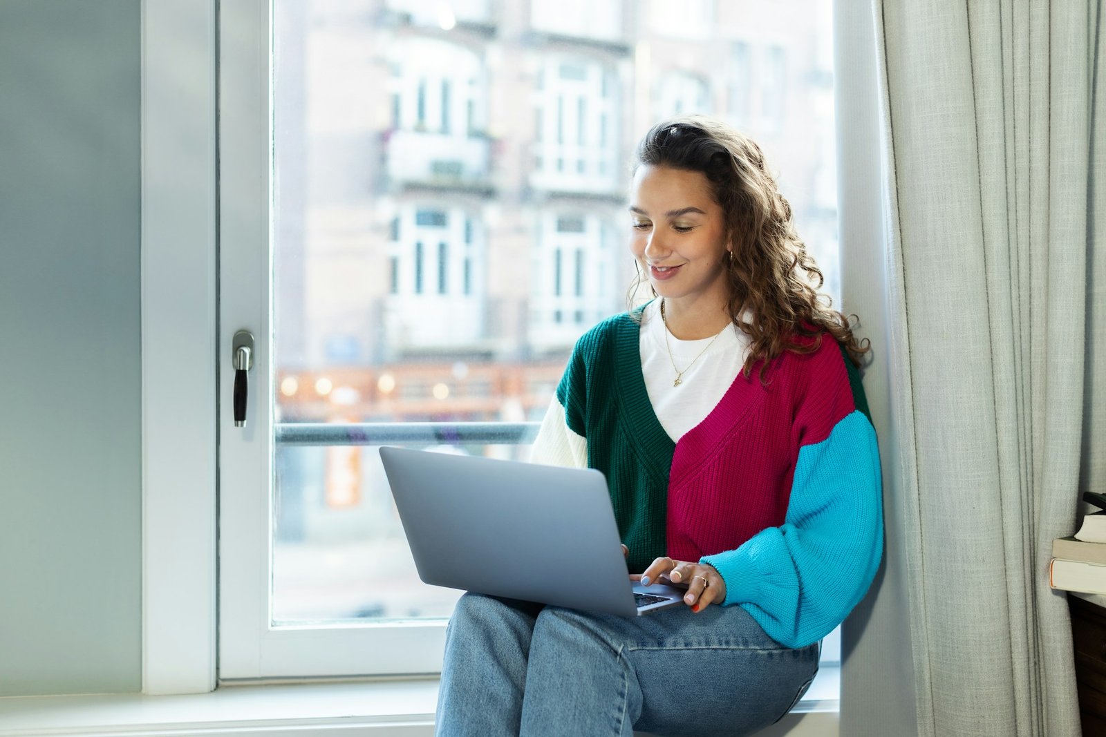 White girl sitting by the window using her laptop